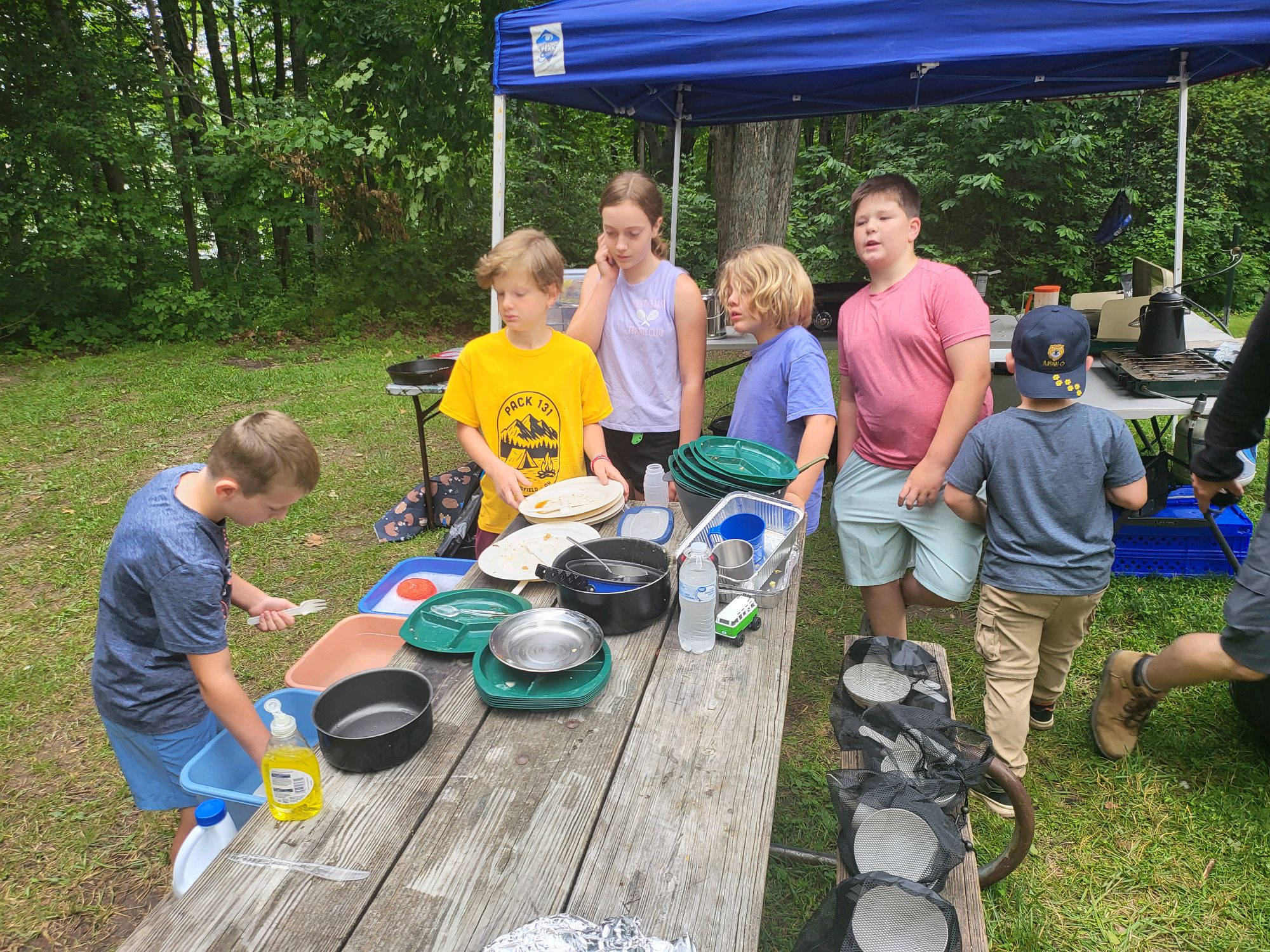 Scouts helping wash dishes and clean up under the blue canopy