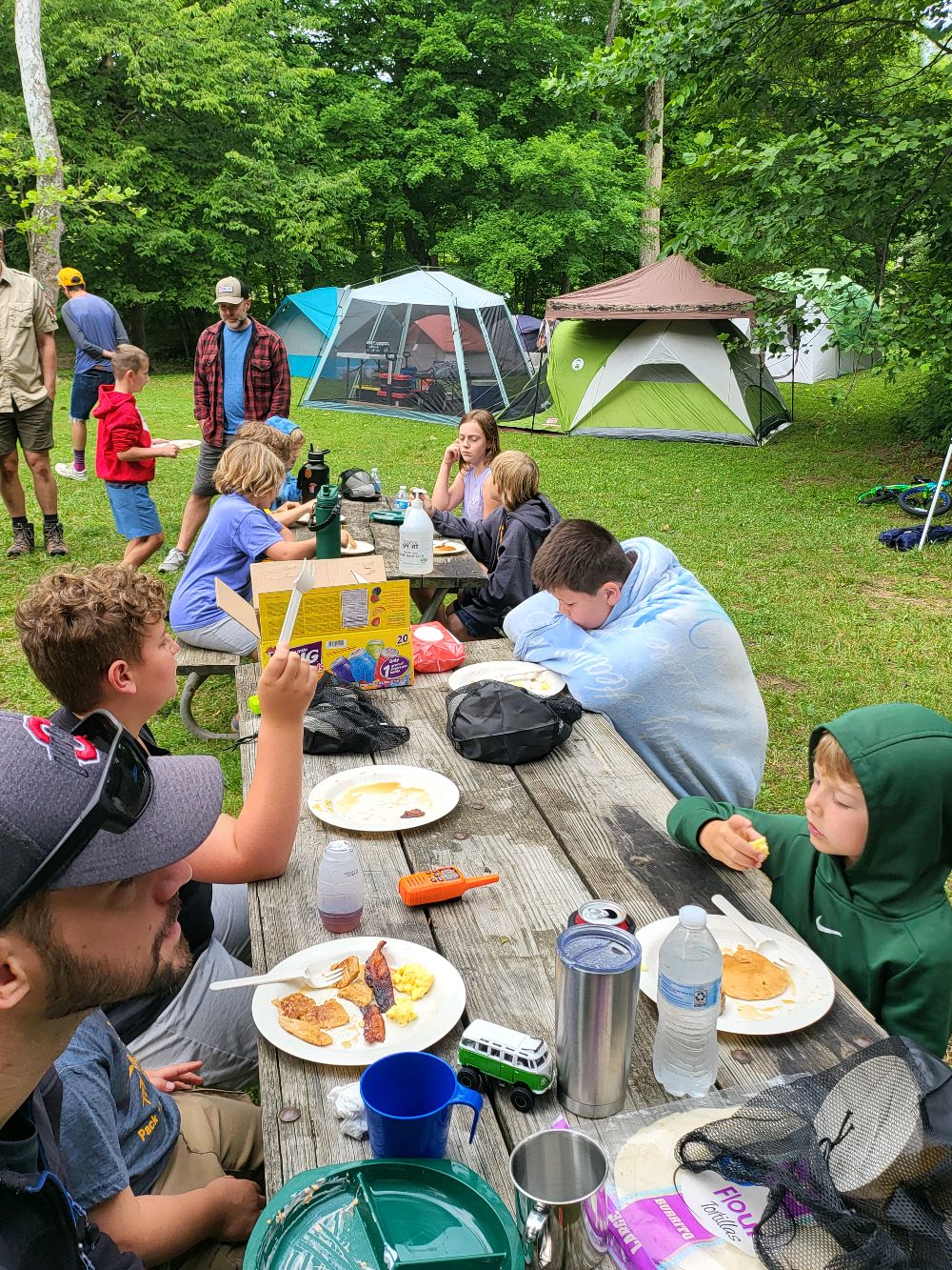 Scouts eating breakfast at a picnic table with tents in the background